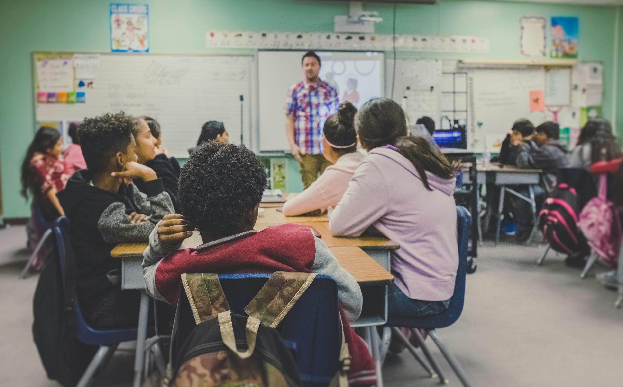 class whole of students sitting at desks and teacher up front 