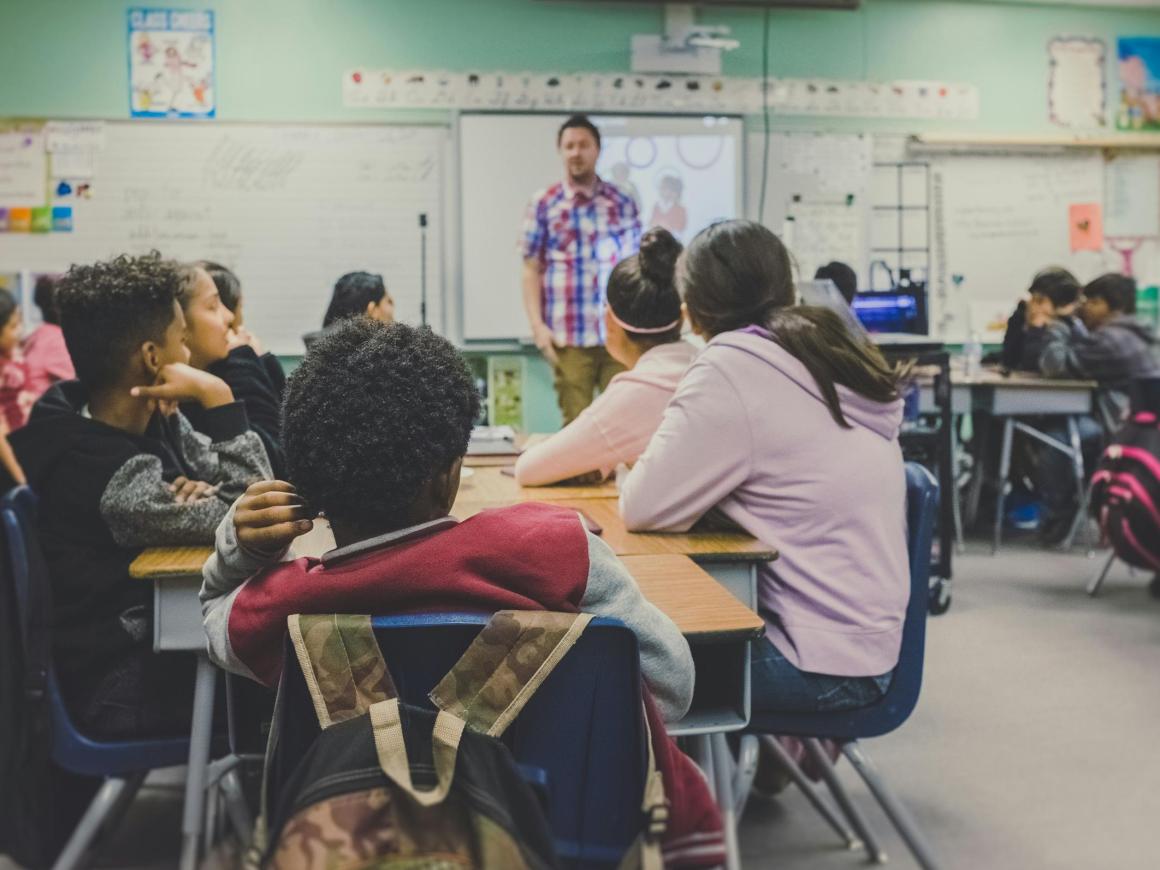 class whole of students sitting at desks and teacher up front 