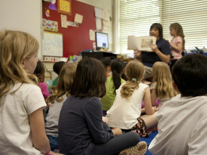 kids sitting on rug while teacher is reading a book