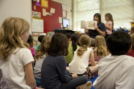 kids sitting on rug while teacher is reading a book