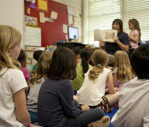 kids sitting on rug while teacher is reading a book