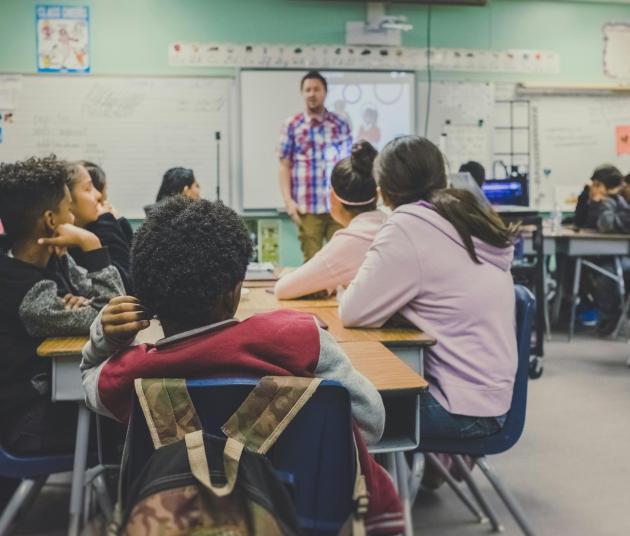 class whole of students sitting at desks and teacher up front 